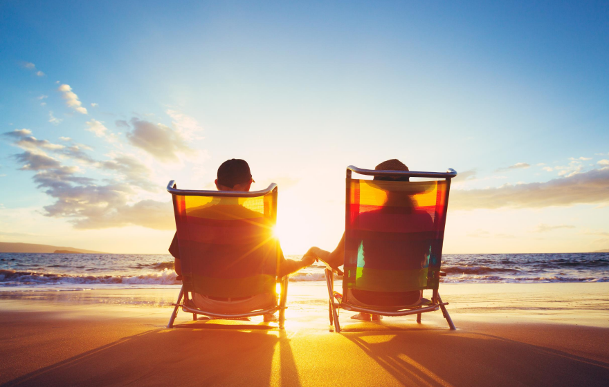 How to boost your superannuation. Middle age couple sitting on beach chairs facing the sunset and holding hands.