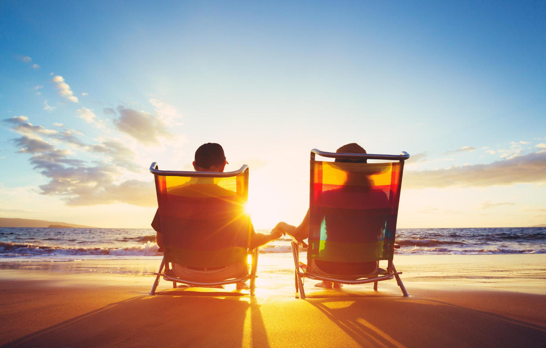 How to boost your superannuation. Middle age couple sitting on beach chairs facing the sunset and holding hands.